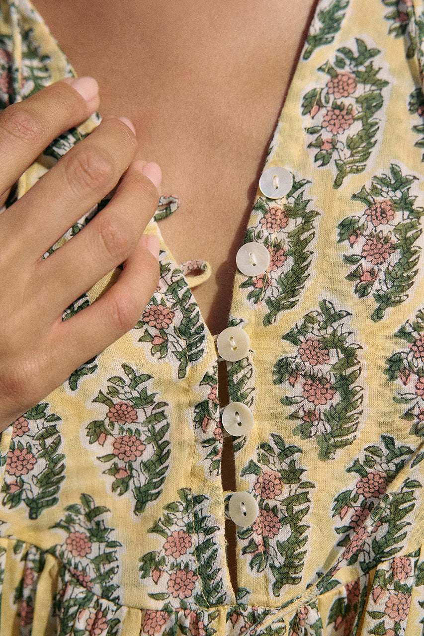 Close-up of V-neckline and button placket on the Daughters of India Bhoomi Mini Dress in Meadow, showing the intricate floral block print fabric on a pale yellow ground