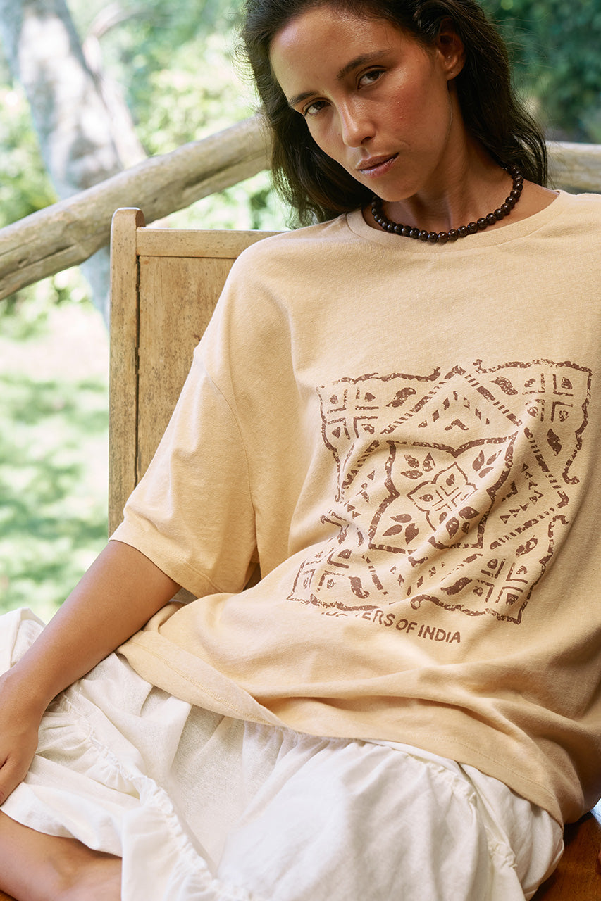 Woman seated outdoors wearing the Daughters of India Shanti Tee in Cashew, an oversized cream block print t-shirt with beaded necklace