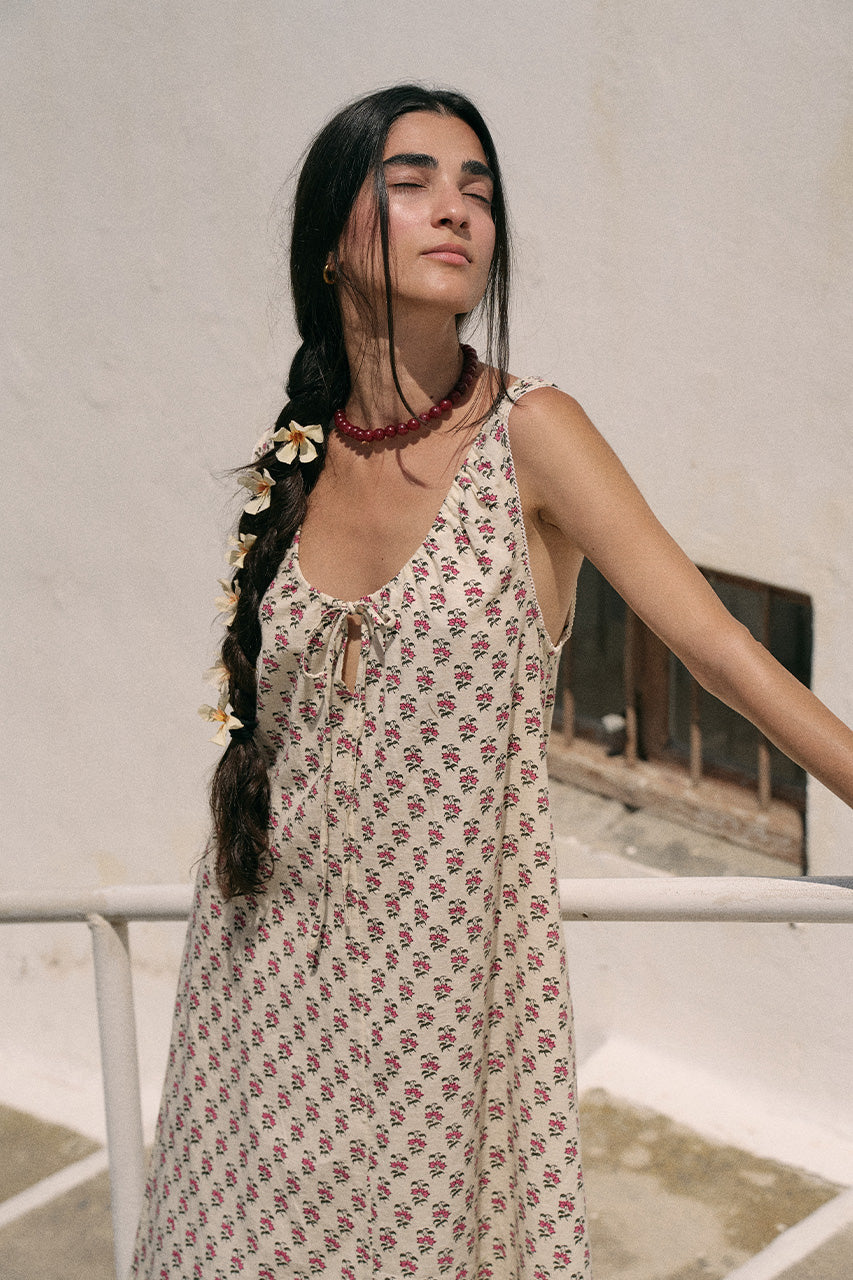 Woman with a braided hair wearing a red beaded necklace and white floral accessories wearing the Daughters of India Sundress Midi in Peony, showing the tie neckline