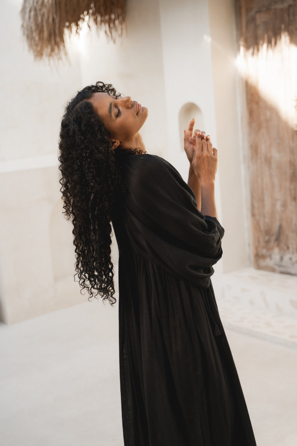 Daughters of India Kyra Midi Dress in Black Gauze — side profile hands raised, billowed sleeves, gathered waist detail